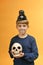 A boy with vampire teeth holds a skull in his hands. Halloween image