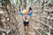 Boy walks across a mesh bridge, holding onto a cable. Back view