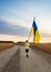 Boy walks along a country road with a yellow-blue Ukrainian large flag among a wheat field