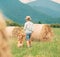 Boy walks with beagle dog on green mountain meadow with haystack