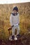 boy in warm clothes stand on chair along a path on a field with dried grass