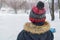 A boy in a warm jacket and woolen hat is in the open air in winter. A rear view