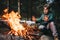 Boy warms his hands near campfire in forest