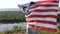 Boy waving national USA flag outdoors over blue sky at the river bank