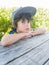 Boy wearing big cap at outside table resting chin