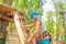 boy wearing blue helmet and climbing equipment climbs the stairs to the round wooden platform in the rope forest