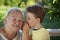 Boy whispering to grandma in summer outdoors garden, grandkid and grandmother lalking