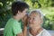 Boy whispering to grandma in summer outdoors garden, grandkid and grandmother lalking