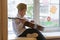 A boy in a white shirt and a Soviet cap sits on the windowsill with a guitar against the background of pasted paper