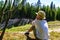 A boy in a white T-shirt and hat sits on the edge of a cliff in the forest and looks thoughtfully into the distance