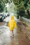 A boy in a yellow raincoat comes out in the rain. child alone walks in the rain. Back view in a bright raincoat.