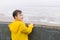 A boy in a yellow raincoat looks at the water surface lake, sea, river, ocean.