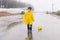 A boy in a yellow raincoat plays a large paper boat in a puddle