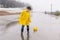 A boy in a yellow raincoat plays a large paper boat in a puddle