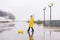 A boy in a yellow raincoat plays a large paper boat in a puddle