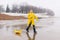 A boy in a yellow raincoat plays a large paper boat in a puddle