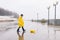 A boy in a yellow raincoat plays a large paper boat in a puddle