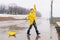 A boy in a yellow raincoat plays a large paper boat in a puddle