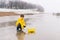 A boy in a yellow raincoat plays and launches in a puddle a large paper boat toy.