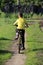 A boy in a yellow T-shirt rides a yellow bike. Picture from the back.