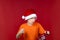 A boy in a yellow T-shirt and a Santa Claus hat holds a gift bag in his hand and shakes his fist at it