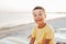 boy in yellow t-shirtsitting on bench near sea alone on beach at sunset. Happy family travel. Summer vacation with child