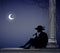 Boy or young man in hat sit near column and play trumpet under the moon light, lonely date, night melody, night player