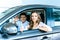 Boyfriend waving a hand, girlfriend showing thumb up sitting in a new car in showroom