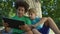 Boys playing tablet sitting under big tree in park, friends spending free time