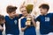 Boys sports team celebrating victory. Happy children holding golden trophy. Kids football team raising winners` cup.  Youth sport