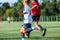 Boys in white and blue sportswear plays football on field, dribbles ball. Young soccer players with ball on green grass.