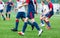 Boys in white and blue sportswear plays football on field, dribbles ball. Young soccer players with ball on green grass. Training