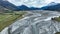 The braided Dart river flowing through a rural valley bordered by the Southern Alps mountains into Lake