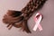 Braided strands and pink ribbon on color background. Concept of hair donation for breast cancer patients