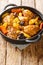 Braised chicken meat with spicy sauce, prunes, carrots, potatoes, olives and onions close-up in a frying pan. Vertical