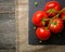 Branch with five ripe red tomatoes. Drops of water on ripe fruits. Green leaves and trunk.