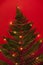 Branch of a forest fern decorated with lighted garland on a bright red background as a alternative christmas tree