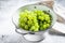 A branch of green ripe grapes in a colander. White background. Top view