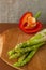 branches of fresh green asparagus on a wooden board, red big pepper on the background. brown background, top view. Basic