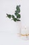 Branches of green silver dollar eucalyptus in ceramic vase, burning candle on white background, styled image