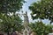 Through the branches and leaves of trees against a blue sky a tall beautiful temple is visible.