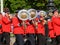 Brass section of marching band in red and blue uniforms passing with large tuba reflecting sun