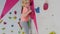 Brave child little blond girl is climbing up artificial wall in rock-climbing gym exercising.