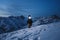 Brave explorer with headlamp commits a night climb to a steep snowy mountain. Wearing ski wear and backpack. Snowboar