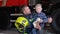 Brave firefighter in uniform holding little saved boy against the background of a fire engine