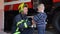 Brave firefighter in uniform and little boy with a toy against the background of a fire engine