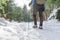 Brave mountaineer woman walking alone with rucksack in the snow, holding a blue stick on the woodland. Walker girl ascend with