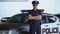 Brave policeman in service cap and sunglasses posing for camera near patrol car