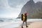 Brave tourist walking by the ocean beach with backpack in front of great mountain rock