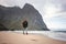 Brave tourist walking by the ocean beach with backpack in front of great mountain rock